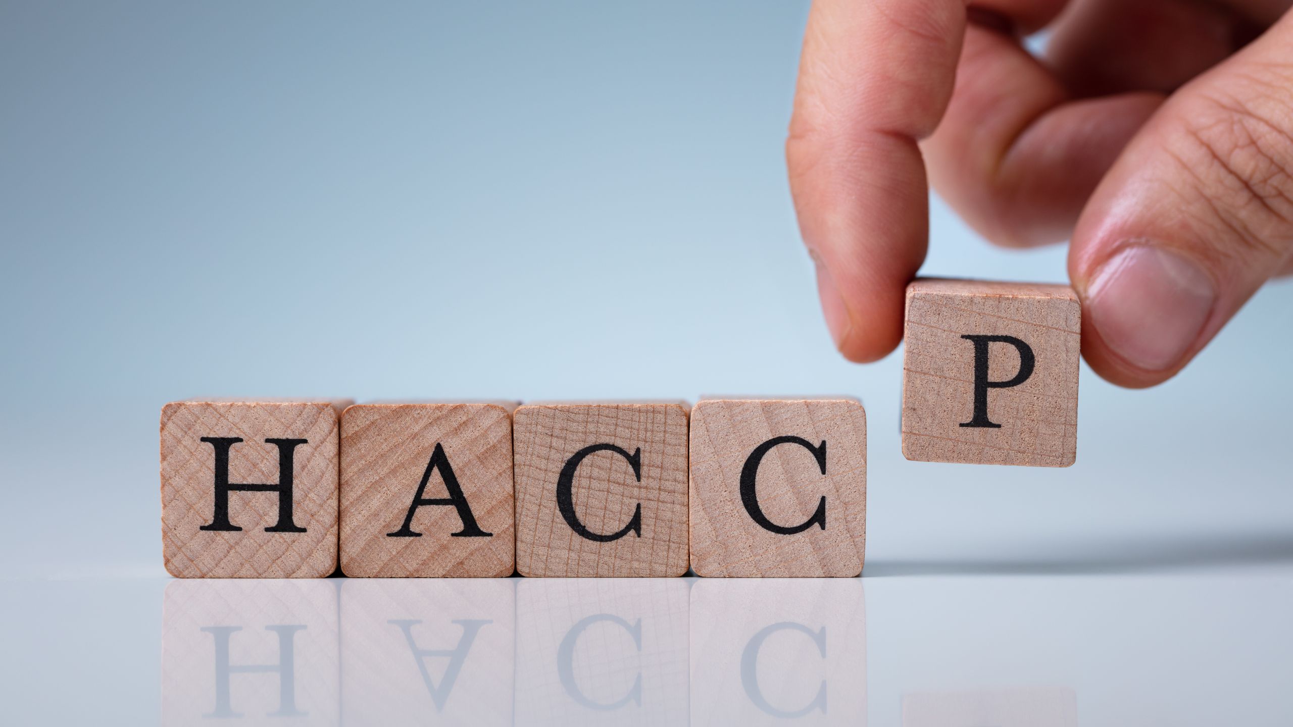 A hand places the final piece to spell out HACCP, representing the PCQI broadening their knowledge.