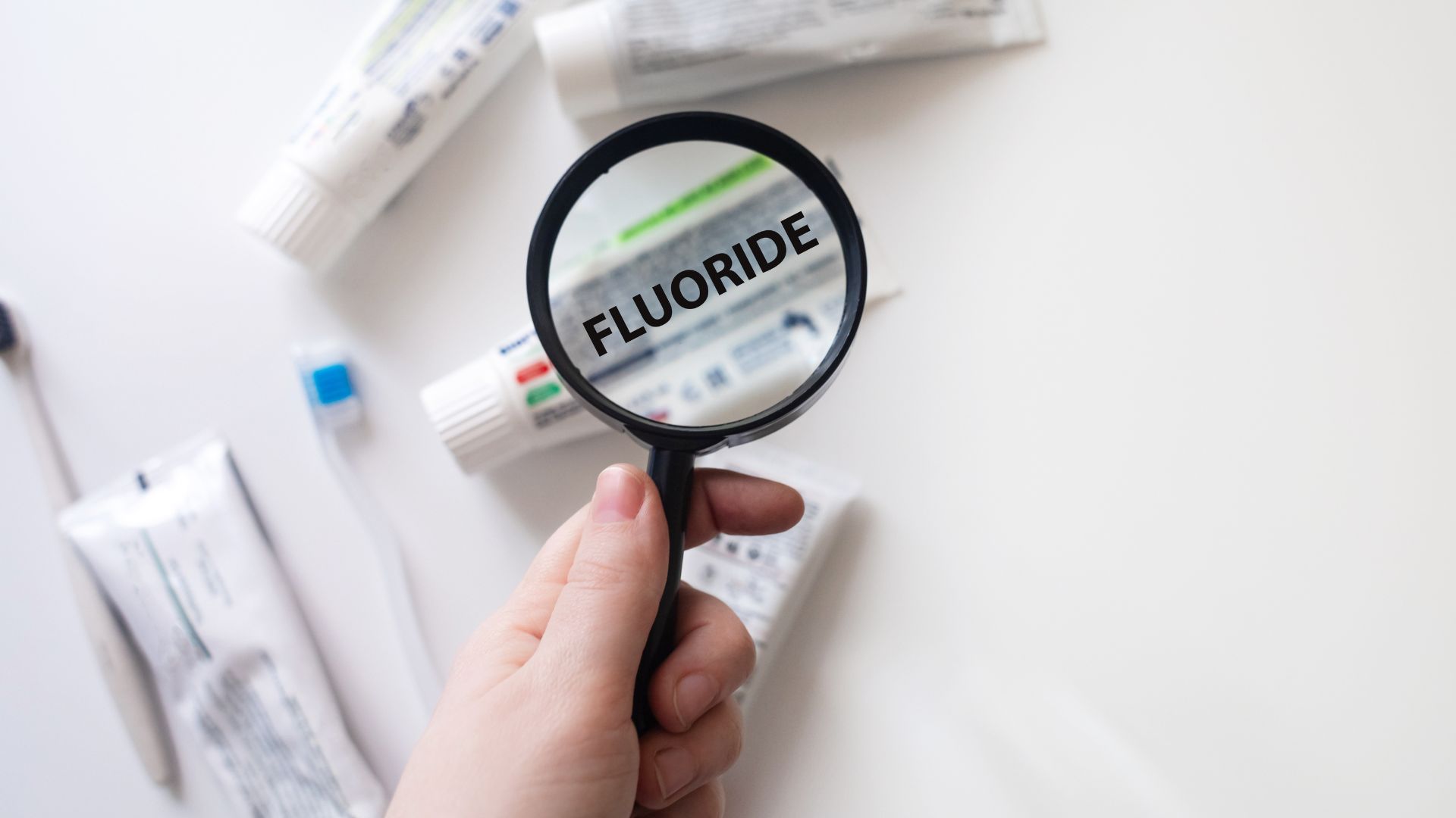 Various tubes of toothpaste containing fluoride are laid out under a magnifying glass.