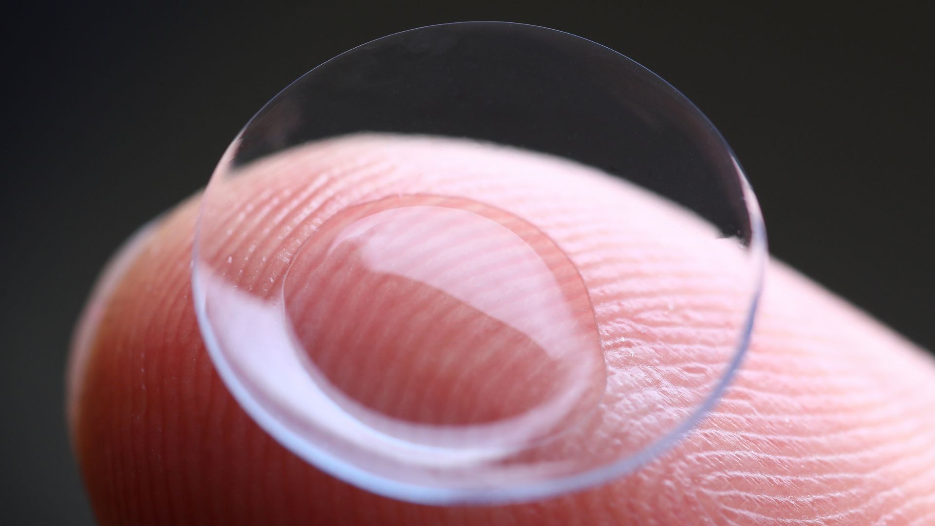 Scleral contact lenses are held close up on a finger.